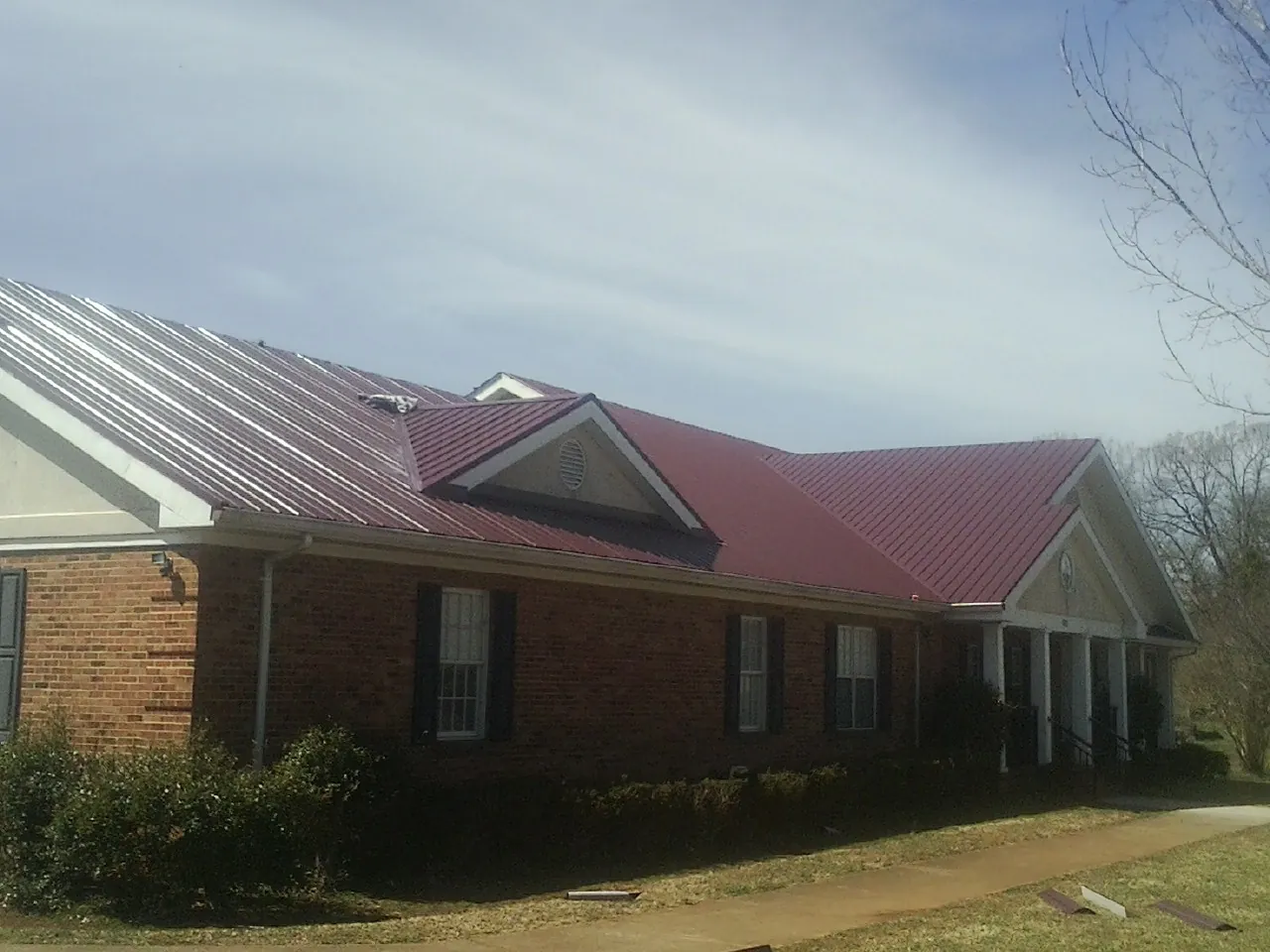 Red metal roof with gabled entries on a long brick building, from a Hail Damage Roof Repair job in Carmel