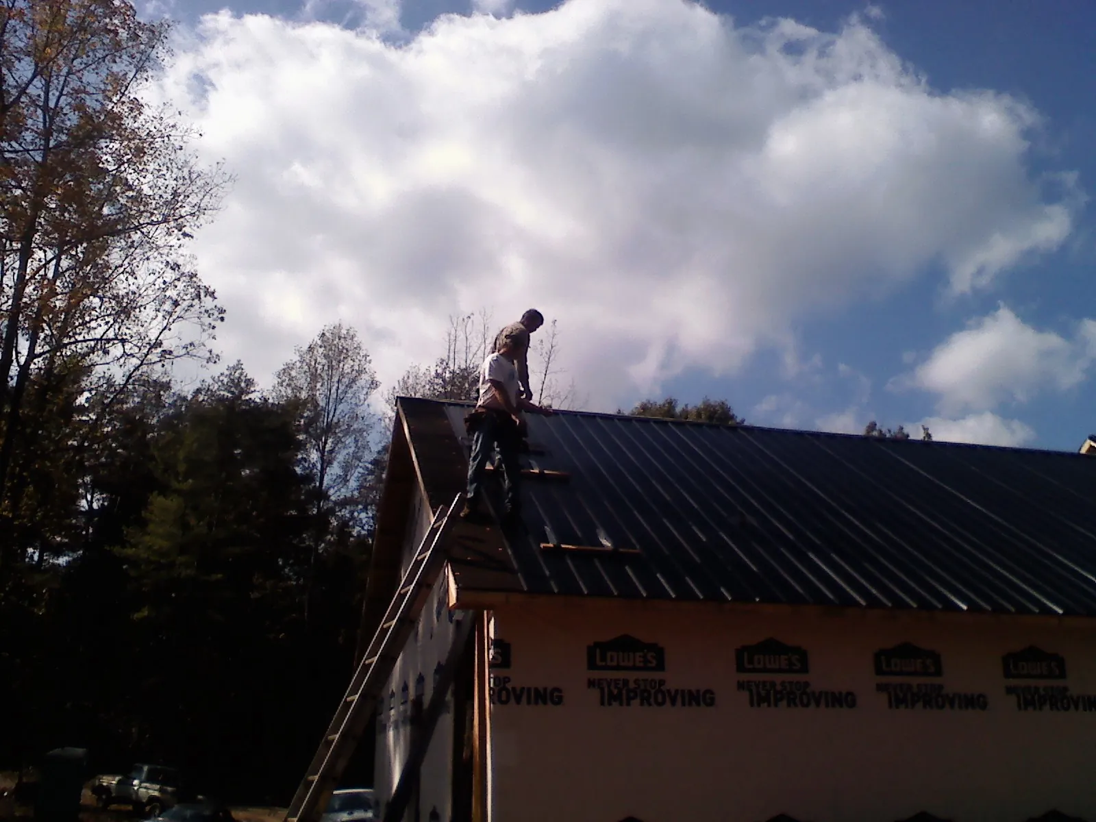 Roofer fastening dark metal panels high against a cloudy sky, from a Roof Inspection job in Carmel